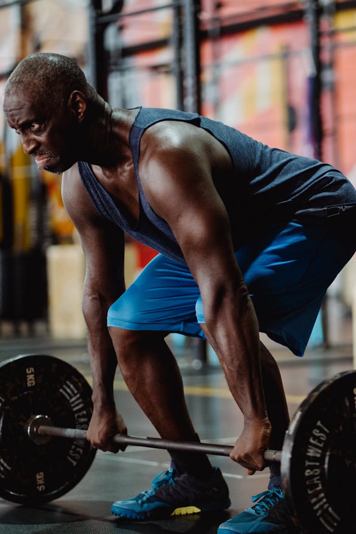 Muscular black male weightlifter performing intense deadlifts in an indoor gym setting.
